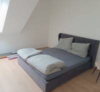 Schlafzimmer in einer Zweizimmerwohnung mit Bett, Holzboden und Dachfenster.