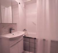 Badezimmer in einer 2-Zimmer-Wohnung mit Waschbecken, Spiegel, Badewanne und weißen Fliesen.