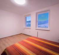 Helles Zimmer mit zwei Fenstern, einem Bett und einem Boden mit Holzdekor.