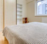 Schlafzimmer in einer Zweizimmerwohnung mit Holzboden, Einbauschrank und großem Fenster.