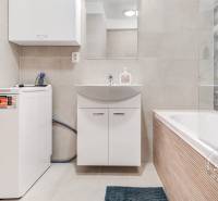 Badezimmer in einer 2-Zimmer-Wohnung mit Badewanne, Waschmaschine und Waschbecken mit Stauraum.