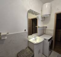 Badezimmer eines Ferienapartments mit Waschmaschine, Waschbecken und Gas-Wassererhitzer.