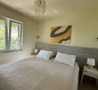 Schlafzimmer im Einfamilienhaus mit Doppelbett, Nachttische mit Lampen, großes Fenster.