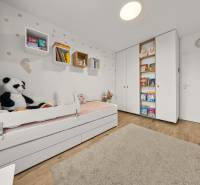 Kinderzimmer in einer Vierzimmerwohnung mit Bett, Spielzeug und Büchern, Boden mit Holzdekor.