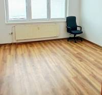 Ein Raum mit einem Boden in Holzoptik, einem Bürostuhl und großen Fenstern.