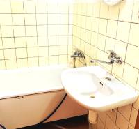 Badezimmer mit Badewanne, Waschbecken und Boden mit Holzdekor in einer 3-Zimmer-Wohnung.