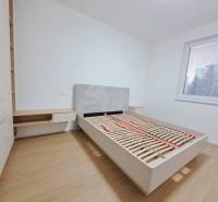 Schlafzimmer in einer 2-Zimmer-Wohnung mit Holzboden, großem Fenster, Bett und Stauraum.