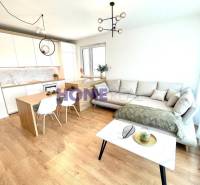 Wohnzimmer mit Küche in einer 3-Zimmer-Wohnung, helle Couch, Boden mit Holzdekor.