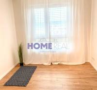 Ein Zimmer mit einem Holzboden und weißen Vorhängen in einer 3-Zimmer-Wohnung.