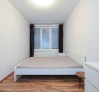 Schlafzimmer in einer 2-Zimmer-Wohnung mit weißen Möbeln und einem Boden in Holzoptik.