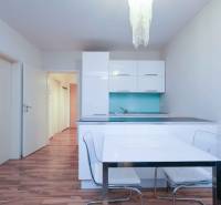 Küche einer Zweizimmerwohnung mit weißen Schränken, blauer Rückwand und Holzboden.