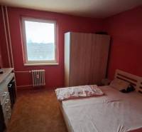 Schlafzimmer in einer 3-Zimmer-Wohnung mit Bett, Schrank und Kommode an der roten Wand.