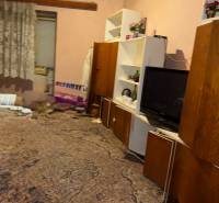 Ein Zimmer in einem Einfamilienhaus mit Teppich, Regalen, Fernseher und Vorhängen.