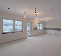 Innenraum in einem Einfamilienhaus mit hellem Boden und großen Fenstern, ohne Möbel.