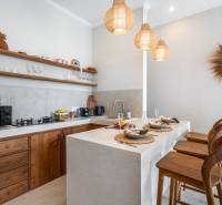 Die Küche der Villa mit stilvollen Holzelementen, Barhockern und Hängelampen.