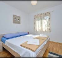 Schlafzimmer in einer 2-Zimmer-Wohnung mit Bett, Holzboden und Fenster mit zarten Vorhängen.
