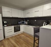 Küche in einer 2-Zimmer-Wohnung mit weißen Schränken und einem Boden in Holzoptik.