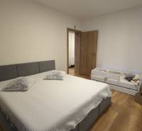 Schlafzimmer mit grauem Bett und Kinderbett, Holzboden in einer 2-Zimmer-Wohnung.