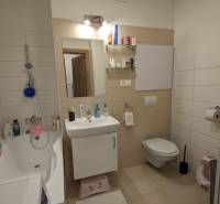 Badezimmer in einer 2-Zimmer-Wohnung mit Badewanne, Waschbecken, Spiegel und heller Wandverkleidung.