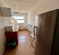 Eine schmale Küche mit Linoleum auf dem Boden, einem Kühlschrank und einem Fenster in den Büros.