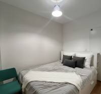Schlafzimmer in einer 2-Zimmer-Wohnung mit weißen Möbeln, grauen Accessoires und einem Sessel.