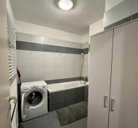 Badezimmer mit Waschmaschine, Badewanne und weißen Fliesen in einer 2-Zimmer-Wohnung.