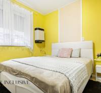 Schlafzimmer im Einfamilienhaus mit gelben Wänden, weißem Bett und Blumendekoration.