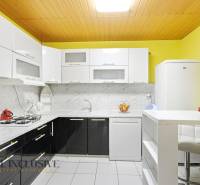 Eine Küche in einem Einfamilienhaus mit hellen Schränken, Marmorverkleidung und weißen Geräten.