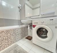 Badezimmer mit Badewanne und Waschmaschine in einer 2-Zimmer-Wohnung, Fliesen und weiße Fliesen.