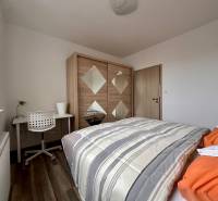 Schlafzimmer in einer 3-Zimmer-Wohnung mit Bett, Schrank, Tisch und Boden in Holzoptik.