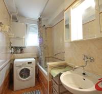 Badezimmer mit Badewanne und Waschmaschine in einer 3-Zimmer-Wohnung, mit cremefarbenen Fliesen.