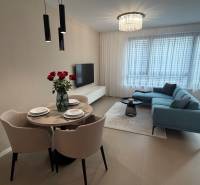 Wohnzimmer in einer Zweizimmerwohnung mit grauem Sofa, Esstisch und Boden in Holzoptik.