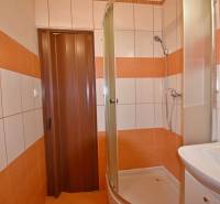 Badezimmer in einem Einzimmerapartment mit Fliesen und Duschkabine, in orange-weißer Ausführung.