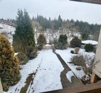 Ein verschneiter Garten eines Einfamilienhauses in Čadca in der Straße Čadečka mit Nadelbäumen und Rasen.