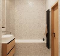 Ein Badezimmer mit hellen Fliesen, einem Holzunterschrank unter dem Waschbecken und einem dunklen Leiterheizkörper.