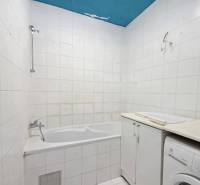 Badezimmer in einer 2-Zimmer-Wohnung mit Badewanne, weißen Fliesen und Waschmaschine.