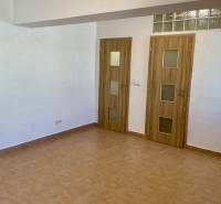 Innenraum einer Einzimmerwohnung mit Keramikboden und zwei Türen mit Holzdekor.