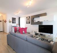 Wohnzimmer in einer Zweizimmerwohnung mit grauem Sofa, Holzboden und Fernseher.