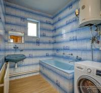 Badezimmer mit Dusche und Waschmaschine in einem Einfamilienhaus. Blaue Fliesen und ein weißer Boiler.