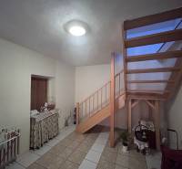 Innenraum eines Einfamilienhauses mit Holztreppe, Tisch und Boden aus Keramikfliesen.