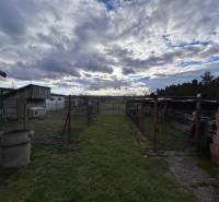 Blick auf den Garten eines Einfamilienhauses in Zbehy mit bewölktem Himmel und Wirtschaftsunterständen.