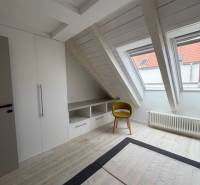 Dachzimmer mit Holzboden, Einbauschrank und gelbem Stuhl.