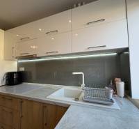 Küche in einer 2-Zimmer-Wohnung mit hellen Schränken und Beleuchtung über der Arbeitsplatte.