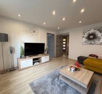 Wohnzimmer in einer 2-Zimmer-Wohnung mit Holzboden, Fernseher und gelbem Sofa.