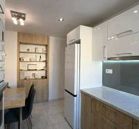 Küche in einer 2-Zimmer-Wohnung mit weißen Schränken, Tisch und Holzdekorregalen.