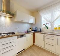 Eine Küche in einem Einfamilienhaus mit weißen Schränken, einem Kühlschrank und einem großen Fenster.