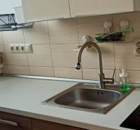 Küche in einer 2-Zimmer-Wohnung mit Spüle, Glaskeramikkochfeld und Korb am Fenster.