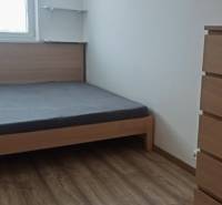 Schlafzimmer in einer 2-Zimmer-Wohnung mit Bett, Holzboden, Kommode und Regalen.