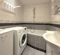 Badezimmer mit Badewanne, Waschmaschine und Fliesen in einer 2-Zimmer-Wohnung.