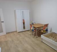 Ein Zimmer in einer 3-Zimmer-Wohnung mit einem weißen Schrank, einem Bett und einem Tisch auf einem Boden mit Holzdekor.